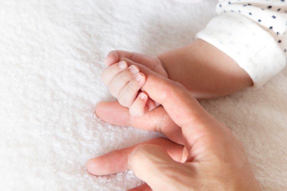 A baby hand grips the finger of an adults hand